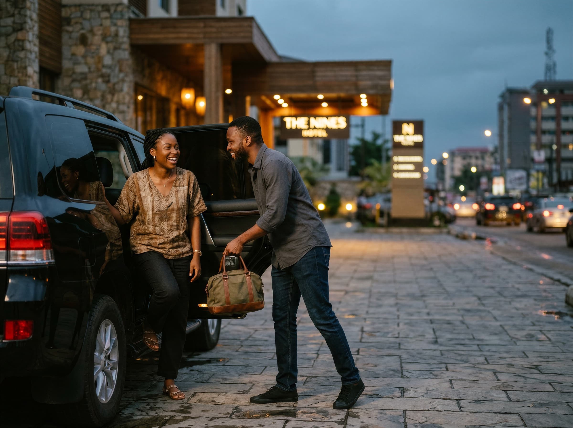 A couple laughing as they step out of a car at a hotel entrance in Lagos at dusk
